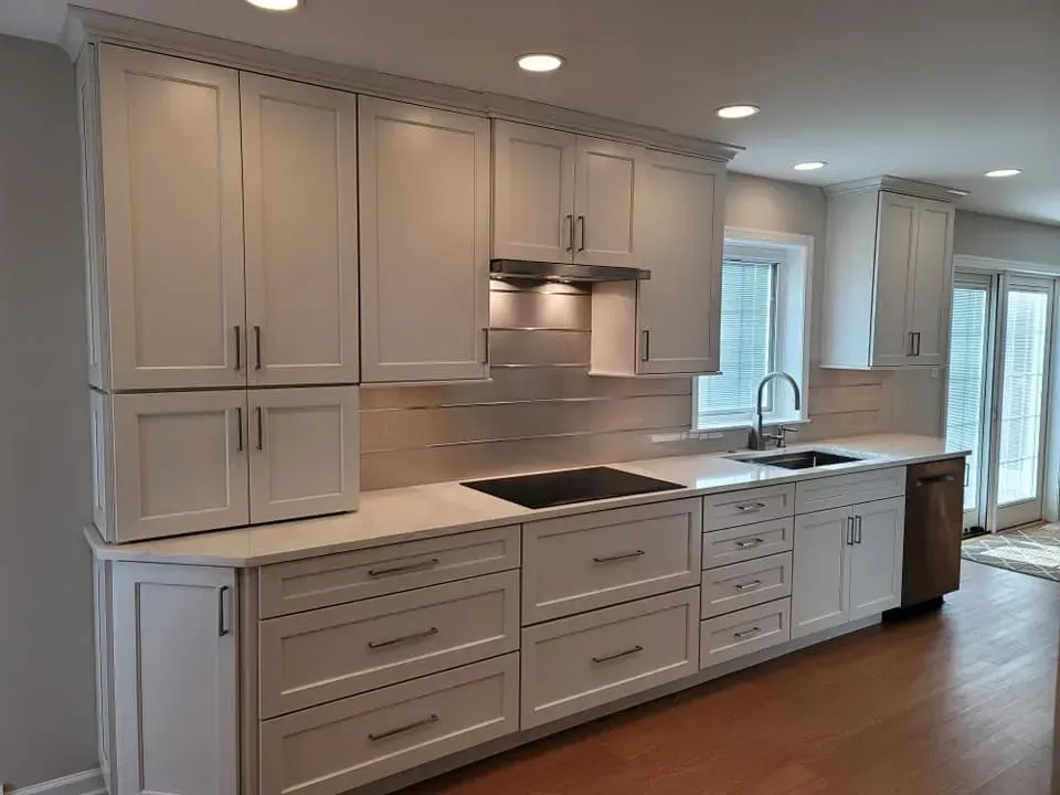 Modern white kitchen with gray cabinets, stainless appliances, and a large island under recessed lights  In Bucks County PA
