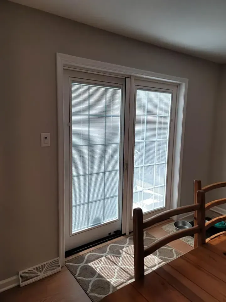 Sunlit glass doors with white blinds in a living room beside a wooden chair and rug  In Bucks County PA