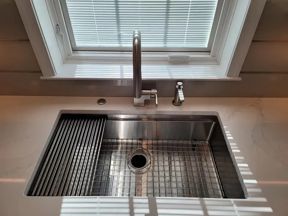 Stainless steel kitchen sink under a window with a chrome faucet and drain rack  In Bucks County PA