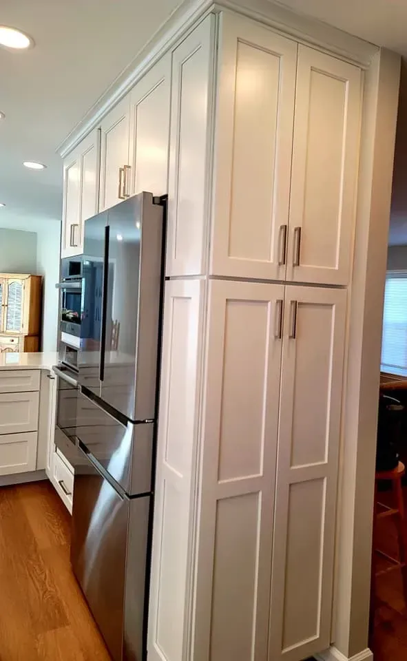 Built-in white kitchen cabinets beside a stainless steel refrigerator in a bright hallway kitchen  In Bucks County PA