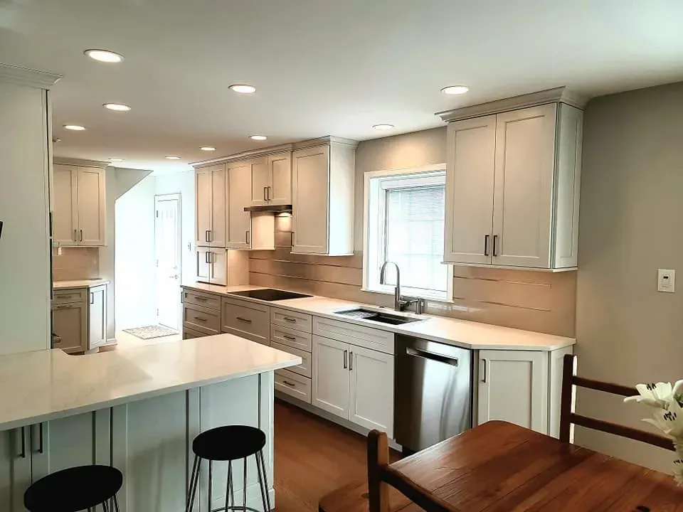 Bright modern kitchen with white cabinets, stainless appliances, and a small breakfast bar with stools In Bucks Country PA