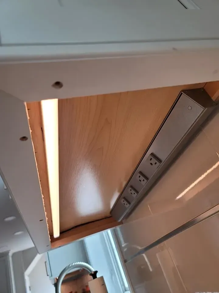 Upward view of a kitchen cabinet underside with wooden panels and a stainless-steel vent hood; a person is partially visible below  In Bucks County PA