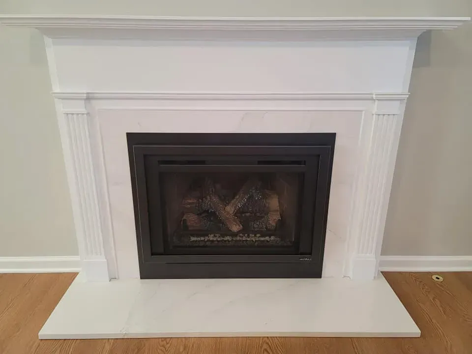 White fireplace mantel with a dark insert and glass front in a light-colored room  In Bucks County PA