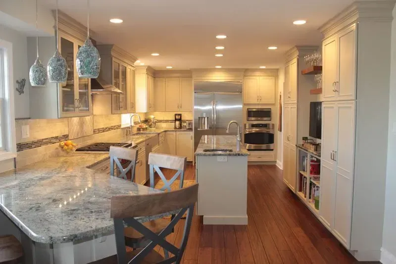 Bright modern kitchen with marble island, pendant lights, white cabinets, and stainless steel appliances In Bucks County PA