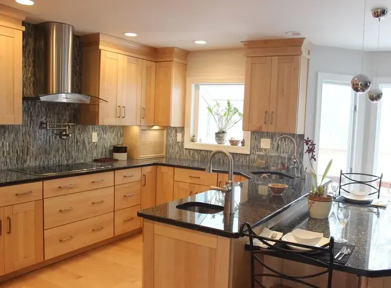 Modern kitchen with light wood cabinets, black countertops, island, and stainless steel range hood In Bucks Country PA
