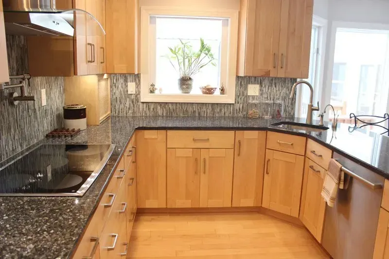 Modern kitchen with wood cabinets, black granite countertops, stainless appliances, and a window over the sink In Bucks Country PA