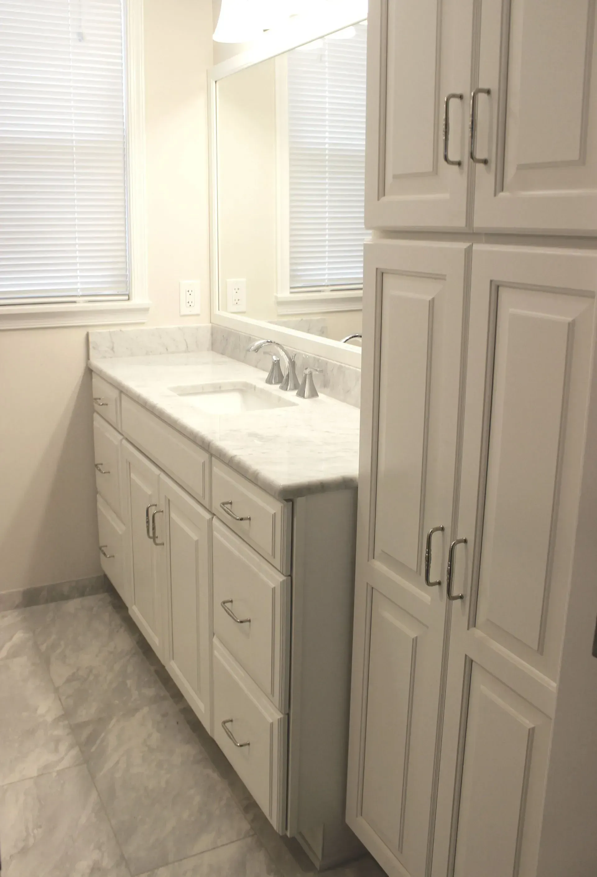 Bright bathroom with white cabinets, marble countertop, large mirror, and windows with blinds In Bucks County PA