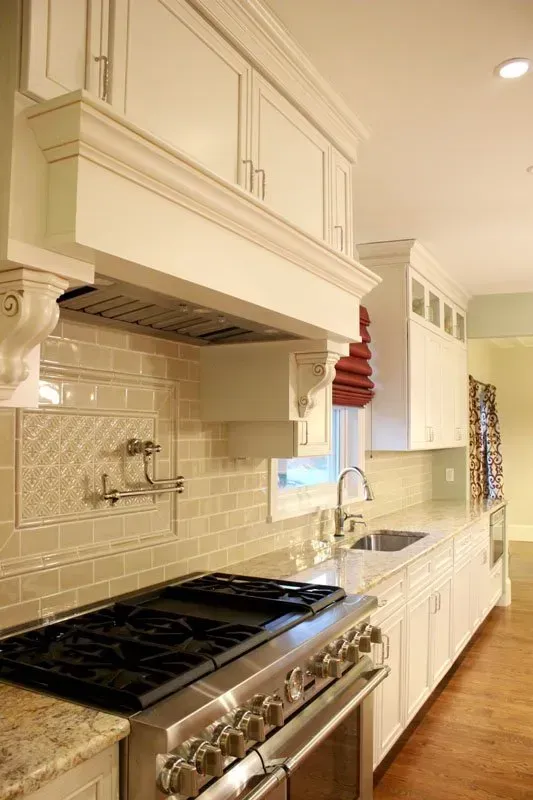 Bright white galley kitchen with stainless range, cream cabinets, tiled backsplash, and hardwood floor In Bucks County PA