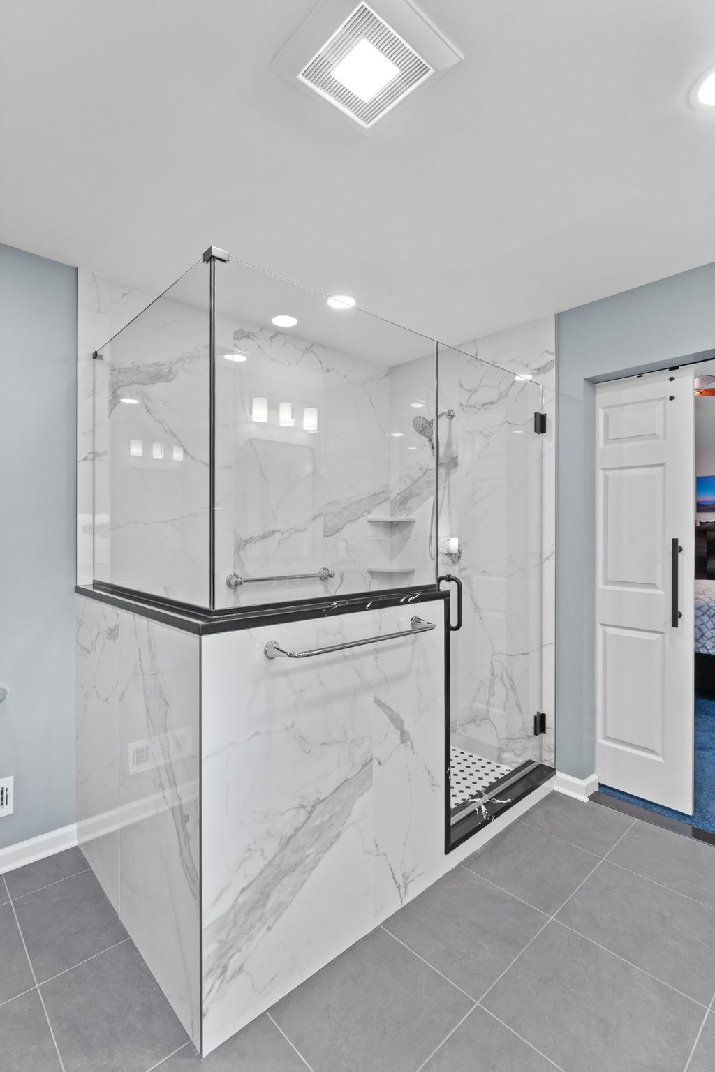Modern bathroom with glass-enclosed shower, gray tile floor, and white marble-style walls In Bucks County PA