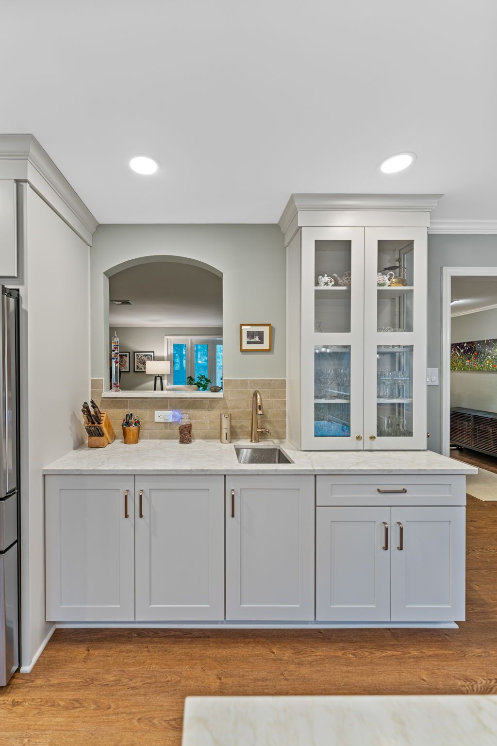 Bright white kitchen with gray cabinets, wood floor, sink, and glass-front pantry cabinet In Bucks County PA