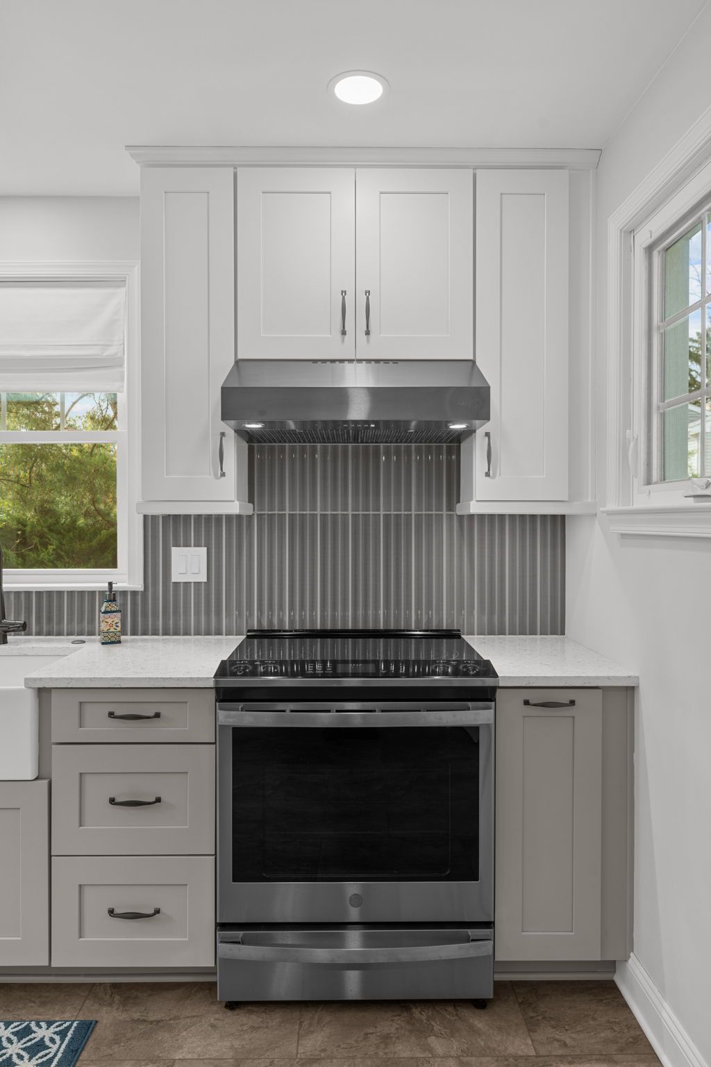 Modern white kitchen with stainless steel stove, white cabinets, and striped backsplash In Bucks County PA