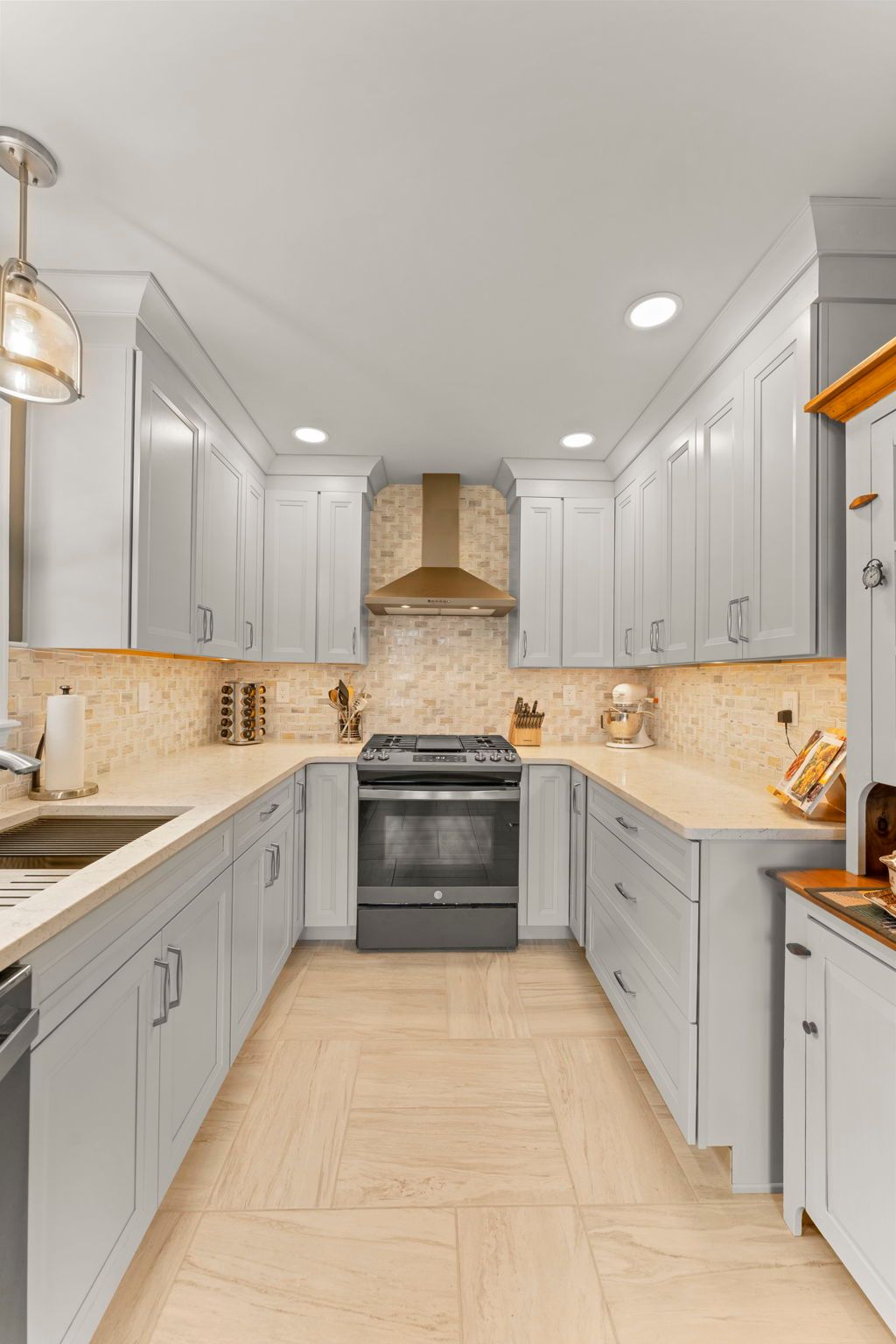 Bright modern kitchen with white cabinets, beige tile backsplash, and stainless steel stove and range hood In Bucks County PA