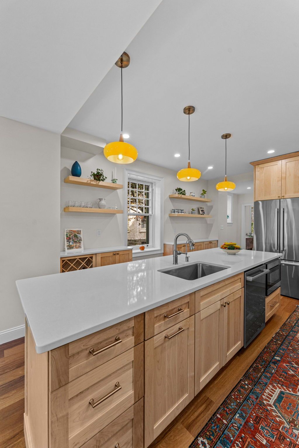 Modern kitchen with white island, wood cabinets, pendant lights, stainless fridge, and patterned rug In Bucks County PA