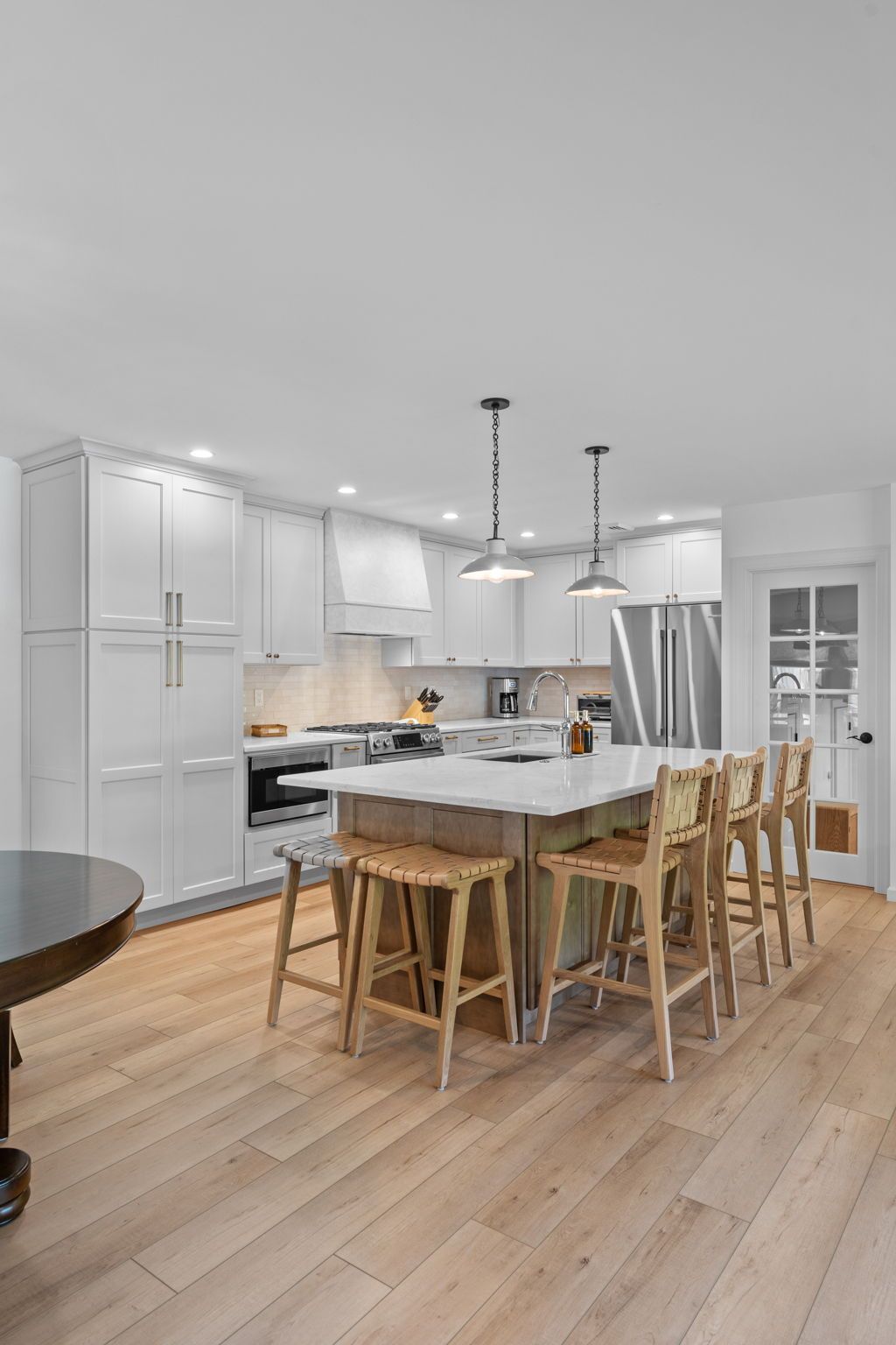 Bright modern kitchen with white cabinets, island, pendant lights, and wooden dining chairs on oak floors In Bucks County PA