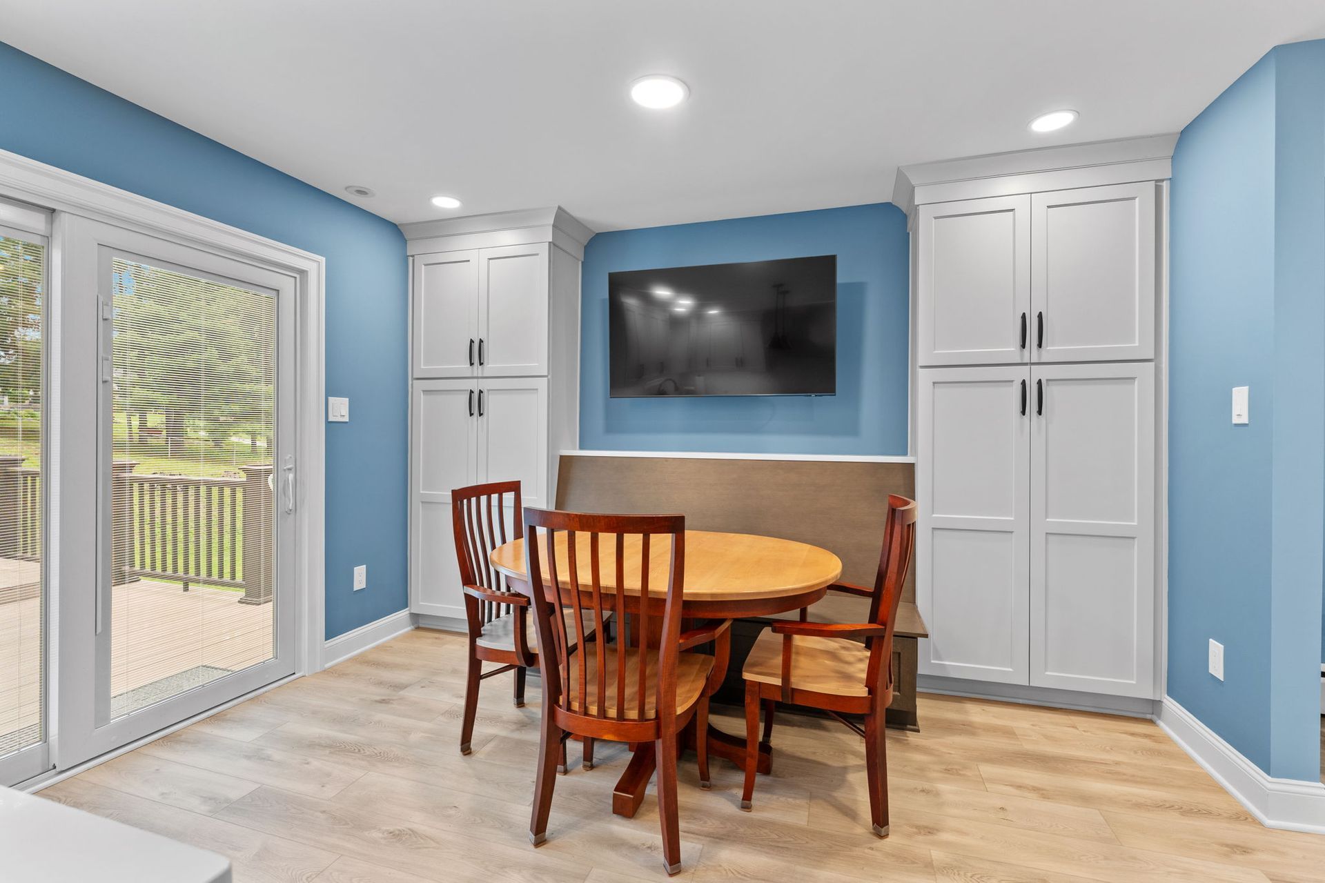 Bright dining room with round wooden table, chairs, blue walls, wall-mounted TV, and glass door to patio in Bucks County PA