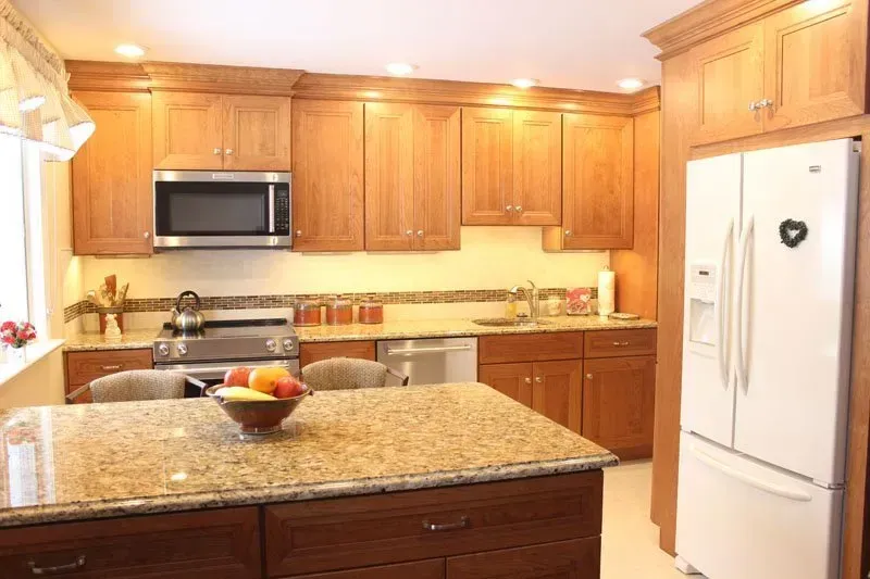 Bright kitchen with wood cabinets, granite island, white refrigerator, and stainless microwave In Bucks Country PA