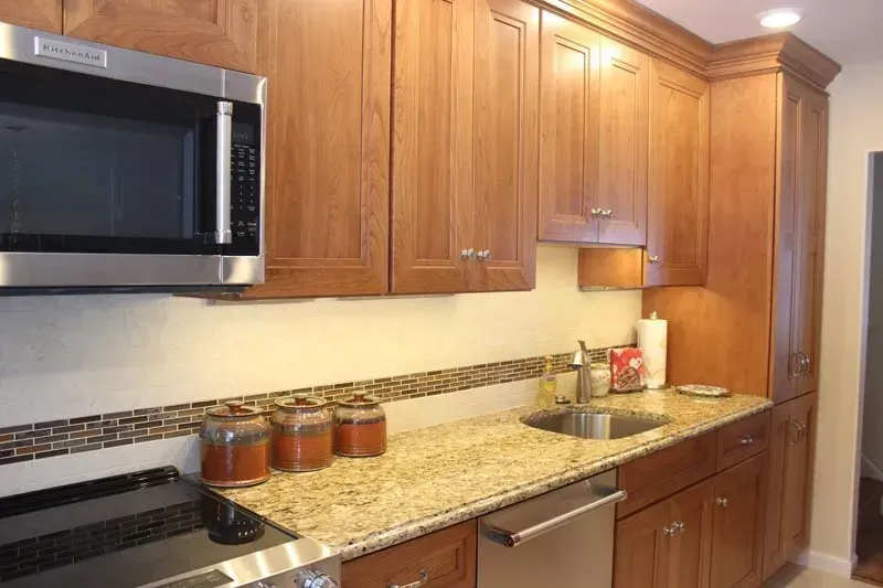 Modern kitchen with wooden cabinets, granite counters, stainless microwave, stove, and sink beneath under-cabinet lighting  In Bucks County PA