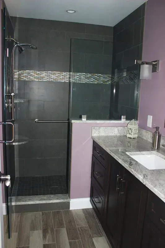 Modern bathroom with dark shower tile, glass door, and dark vanity with marble countertop in Bucks Country PA