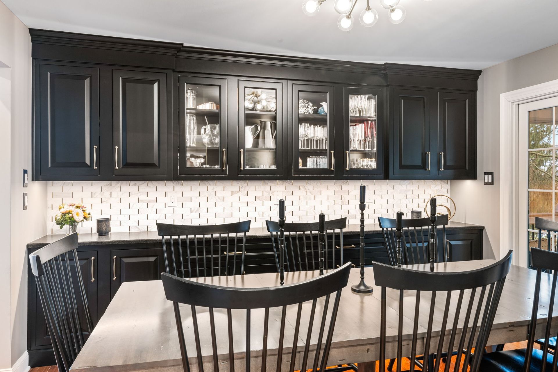 Modern kitchen with black cabinets, white backsplash, island seating, and glass-front cabinets displaying dishes In Bucks County PA