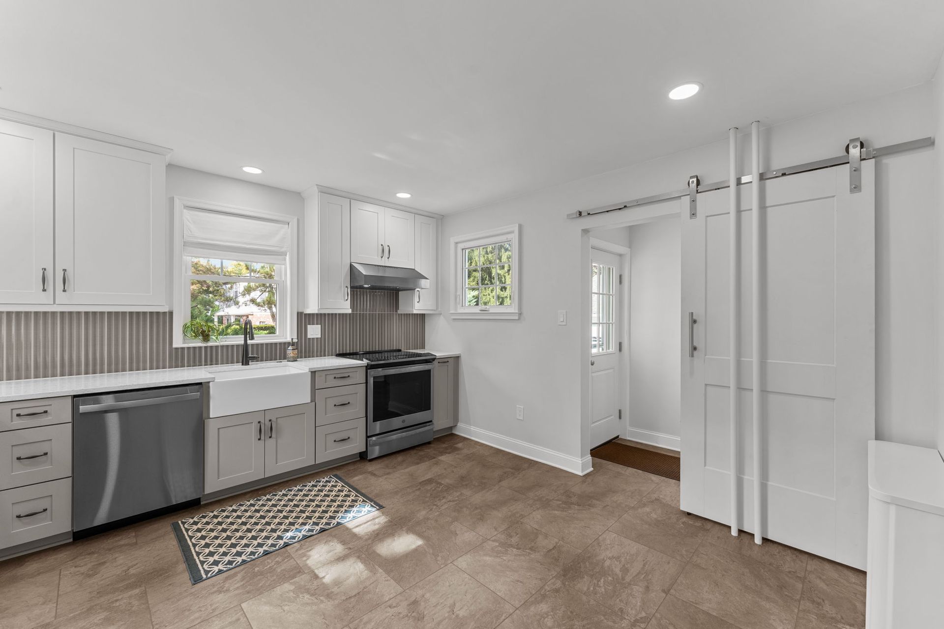 Bright white kitchen with gray cabinets, stainless appliances, beige carpet, and sliding barn door In Bucks County PA