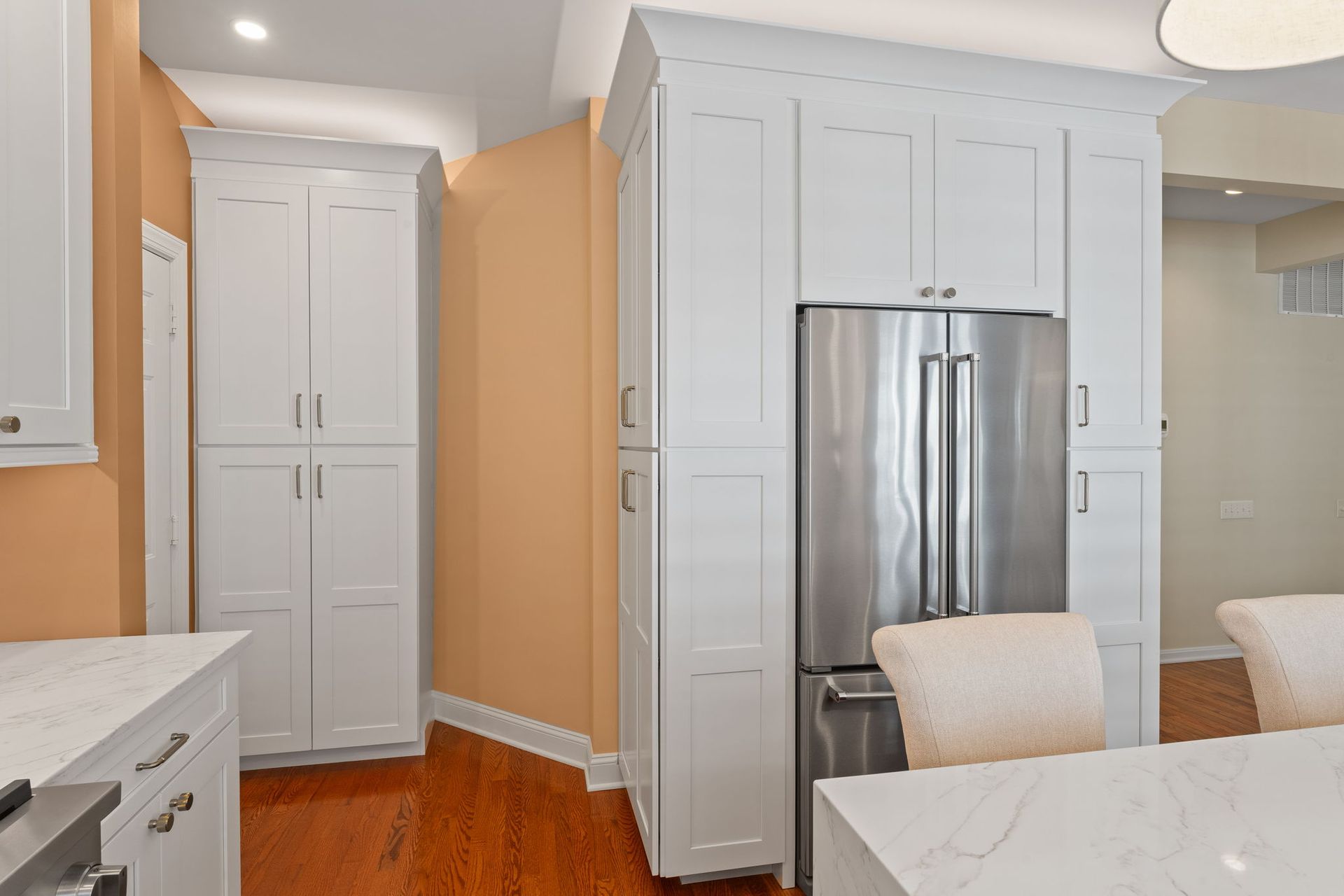 Modern kitchen with white cabinets, stainless steel fridge, and orange accent wall In Bucks County PA
