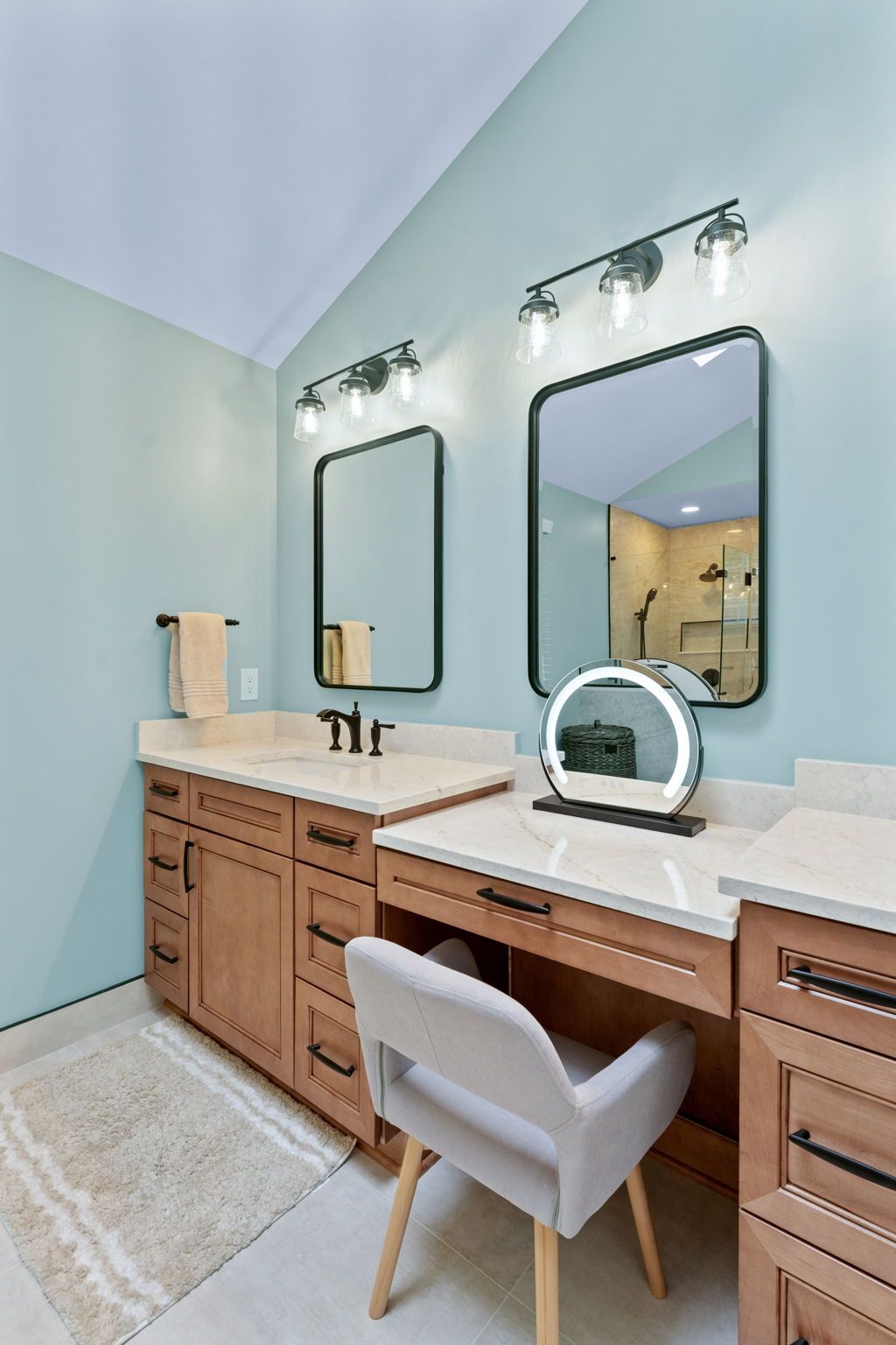 Modern bathroom vanity with double mirrors, wood cabinets, marble countertop, and white chair, in soft blue tones In Bucks County PA