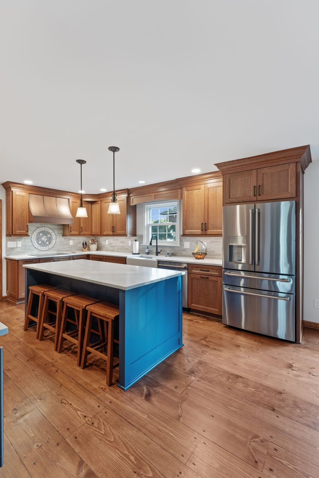 Modern kitchen with a blue island, wooden stools, stainless steel appliances, and wood flooring In Bucks County PA