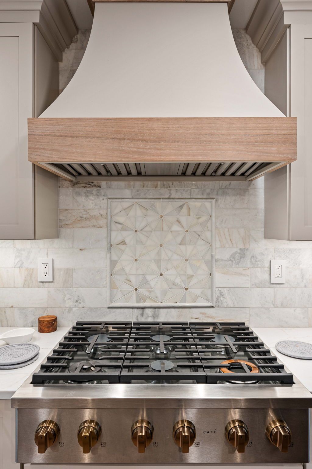 Stainless steel gas range under a white hood with brass knobs and marble tile backsplash in a kitchen in Bucks County PA