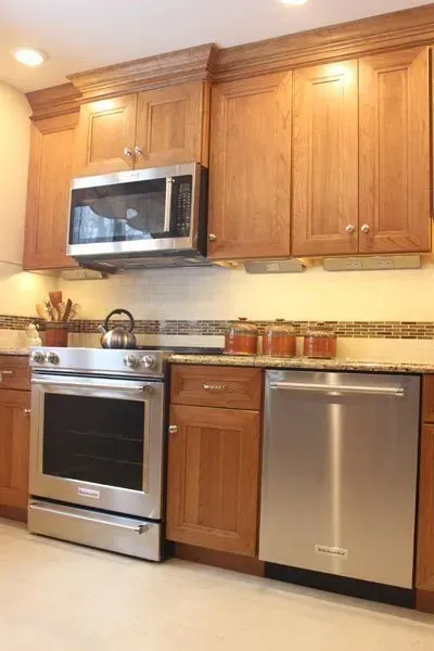Modern kitchen with stainless steel appliances, wood cabinets, and beige tile backsplash  In Bucks County PA