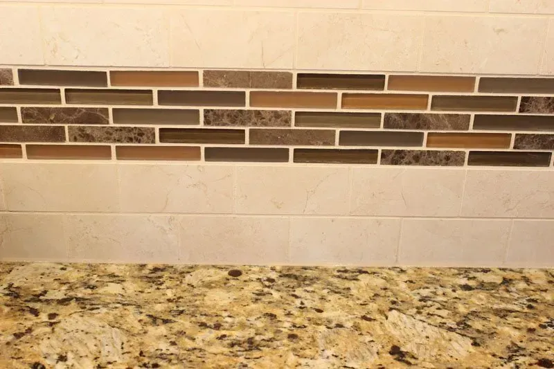 Kitchen backsplash with beige tile, dark mosaic accent band, and granite countertop  In Bucks County PA