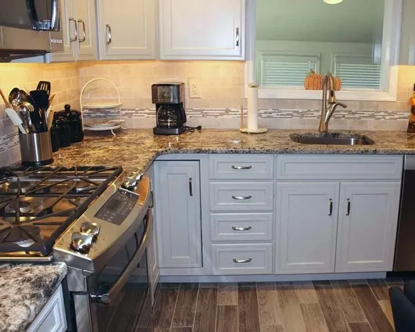 Modern kitchen with granite countertops, gas stove, gray cabinets, and a window over the sink In Bucks County PA