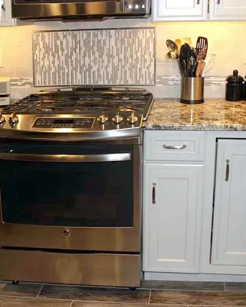 Stainless steel stove beside white cabinets and speckled countertop in a modern kitchen In Bucks County PA