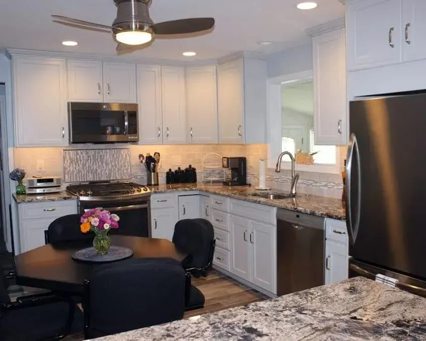 Bright modern kitchen with white cabinets, granite counters, stainless appliances, and a black dining table with flowers In Bucks County PA
