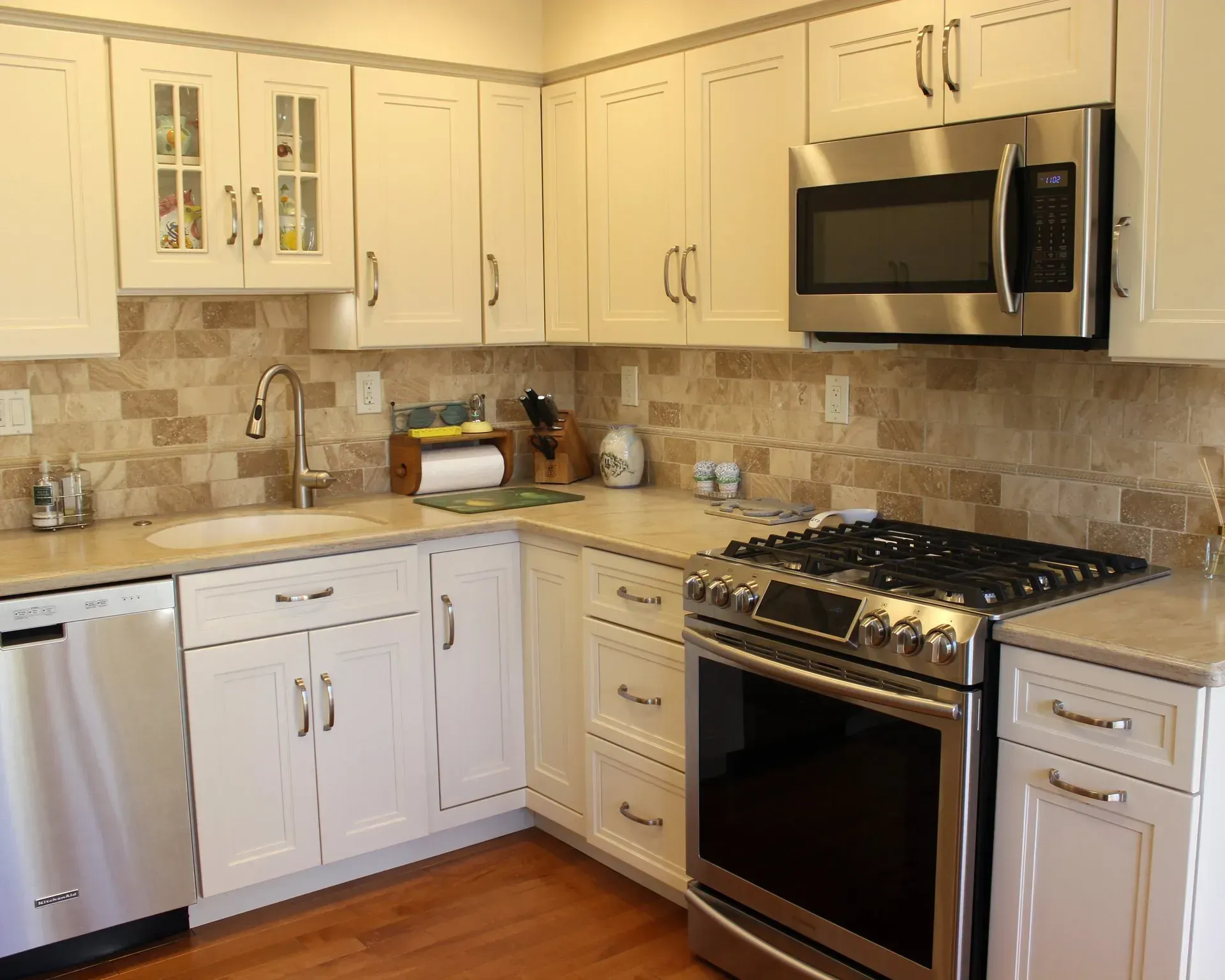 Bright kitchen with white cabinets, stainless steel appliances, beige tile backsplash, and wood floor In Bucks Country PA