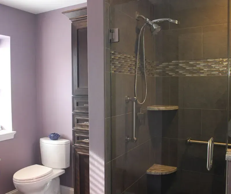 Bathroom with toilet, white sink, and glass-enclosed shower with dark tile and built-in shelves in Bucks Country PA