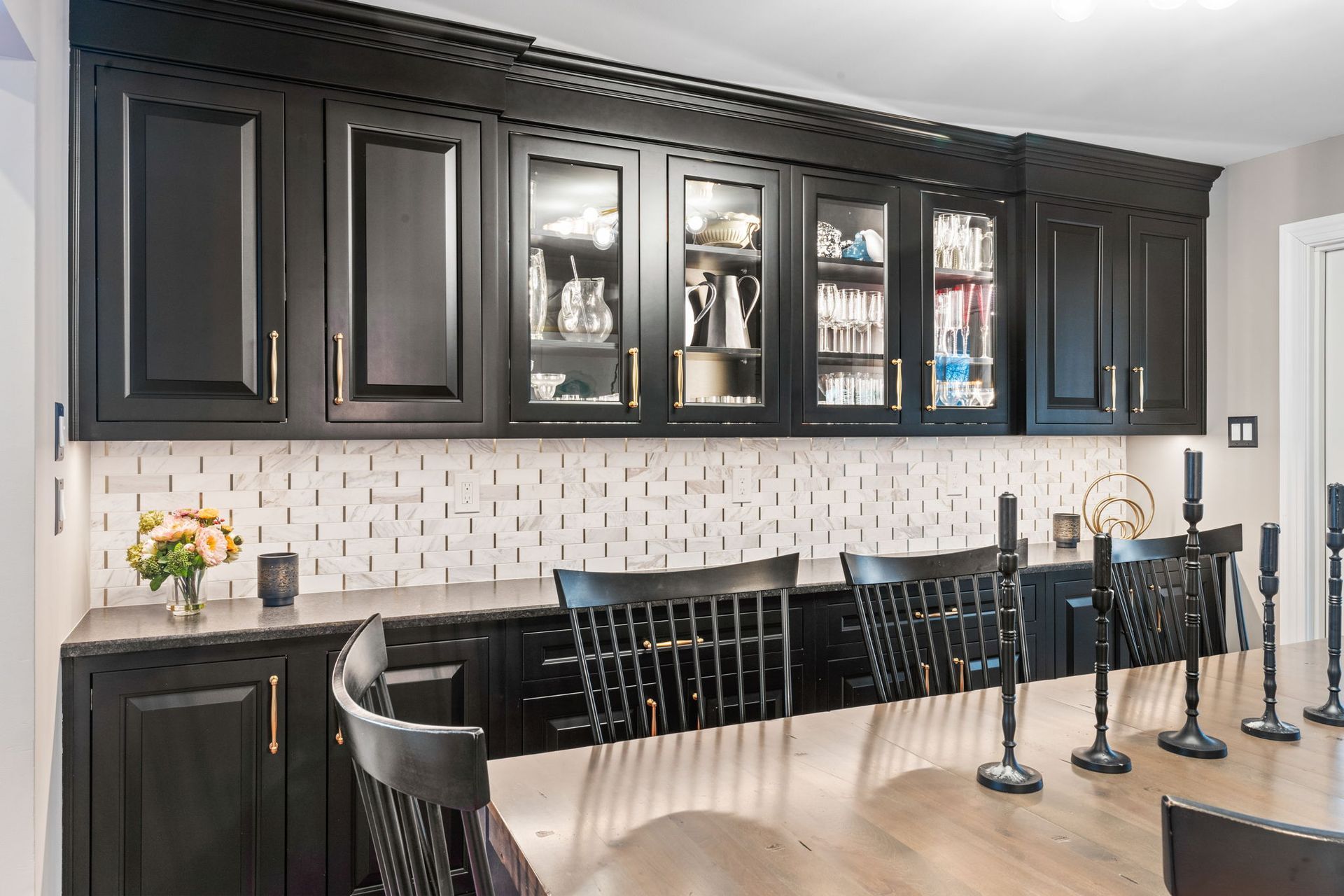Elegant kitchen with dark cabinets, glass-front display, and a long black countertop with bar stools  In Bucks County PA