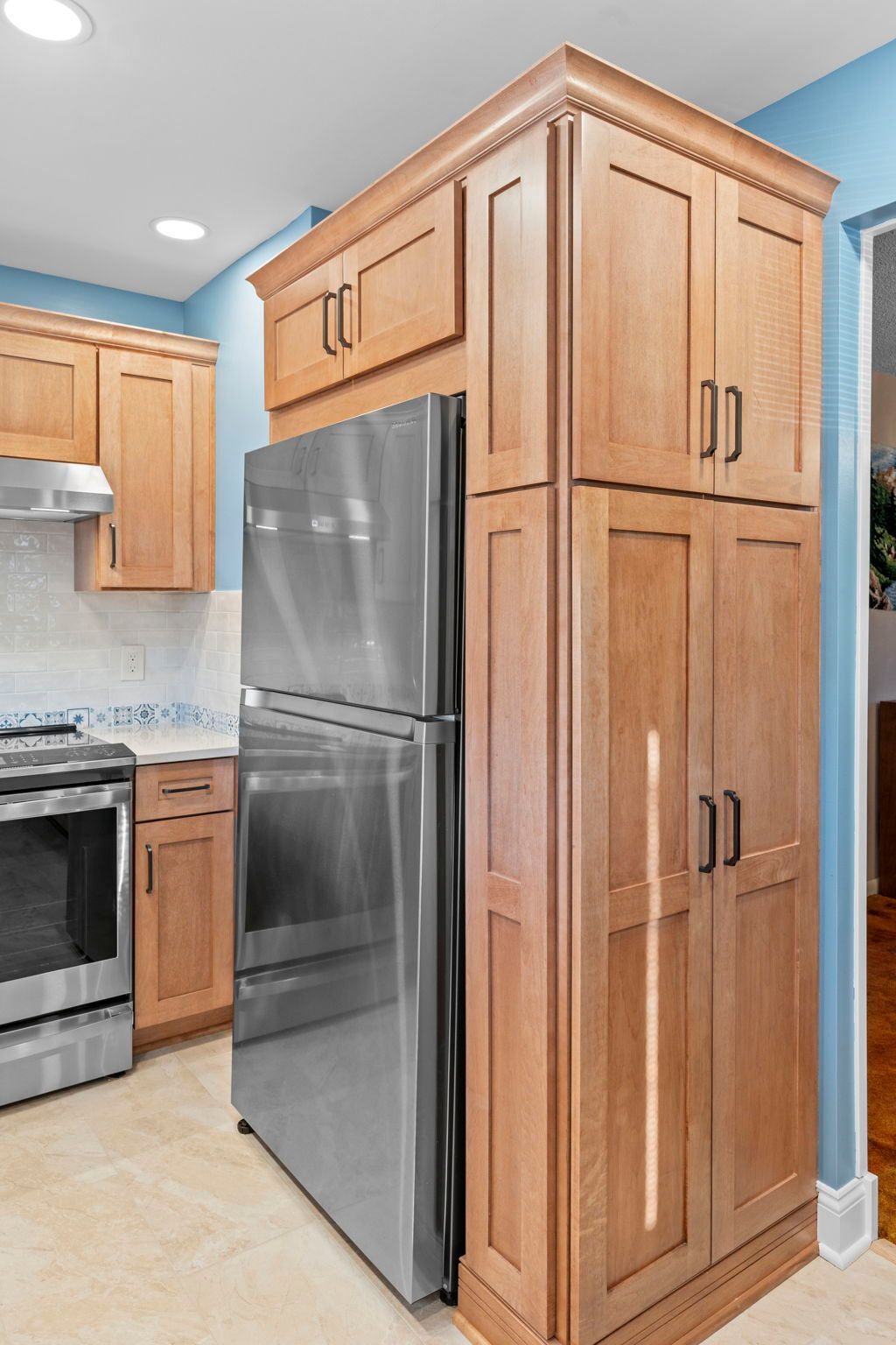 Kitchen with stainless steel fridge beside tall wooden pantry cabinets and a stove in the background In Bucks County PA