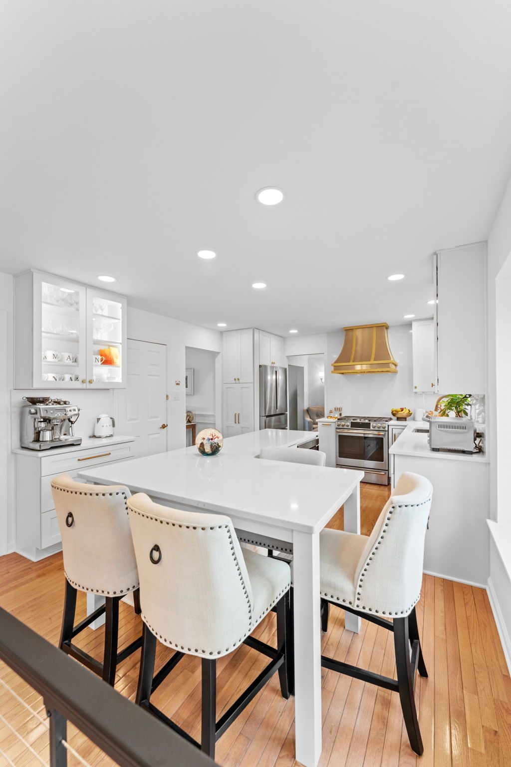 Bright modern kitchen with white island, beige stools, wood floors, and gold pendant light In Bucks Country PA