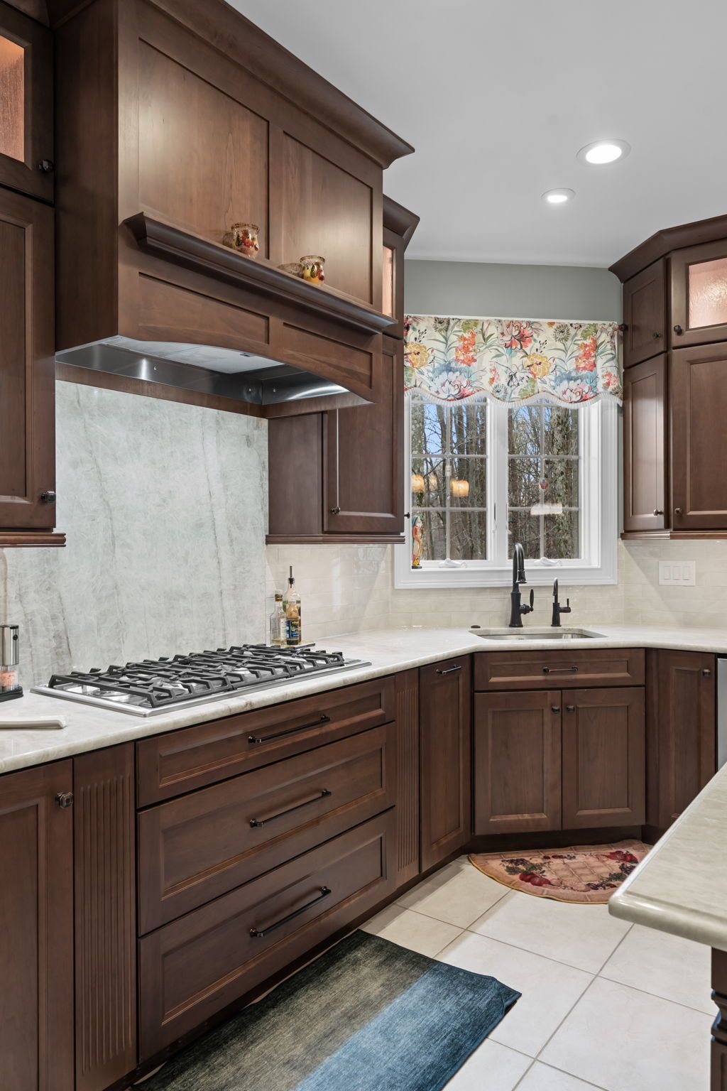 Dark wood kitchen with gas range, white tile backsplash, sink under a window, and tiled floor In Bucks Country PA