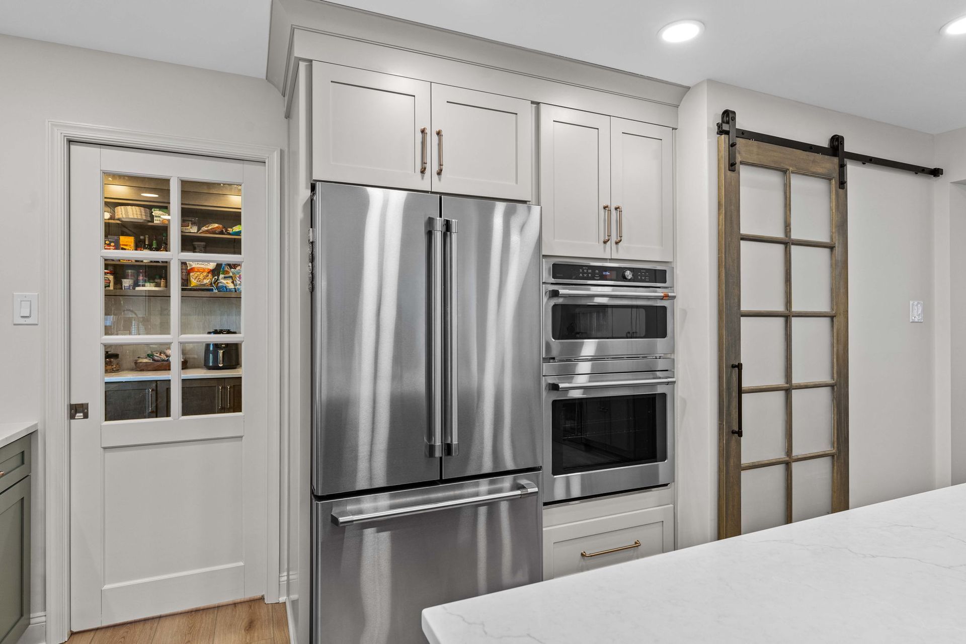 Bright modern kitchen with stainless steel refrigerator, built-in oven, and glass-paned pantry door in Bucks County PA