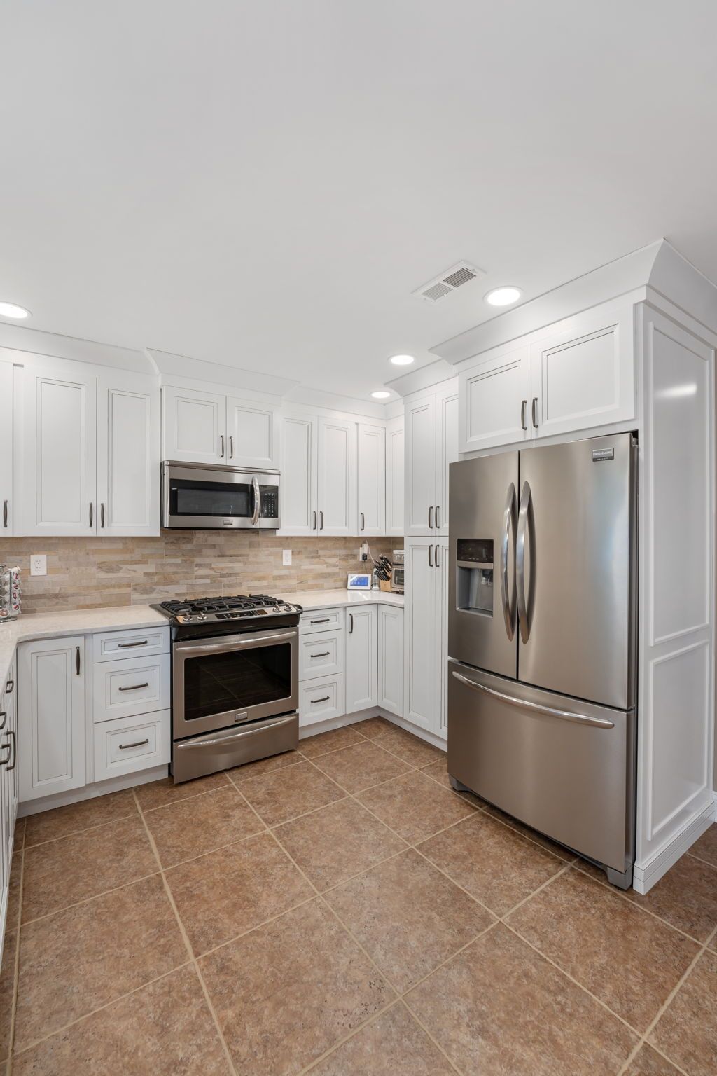 Bright white kitchen with stainless steel appliances and tan tiled floor In Bucks County PA