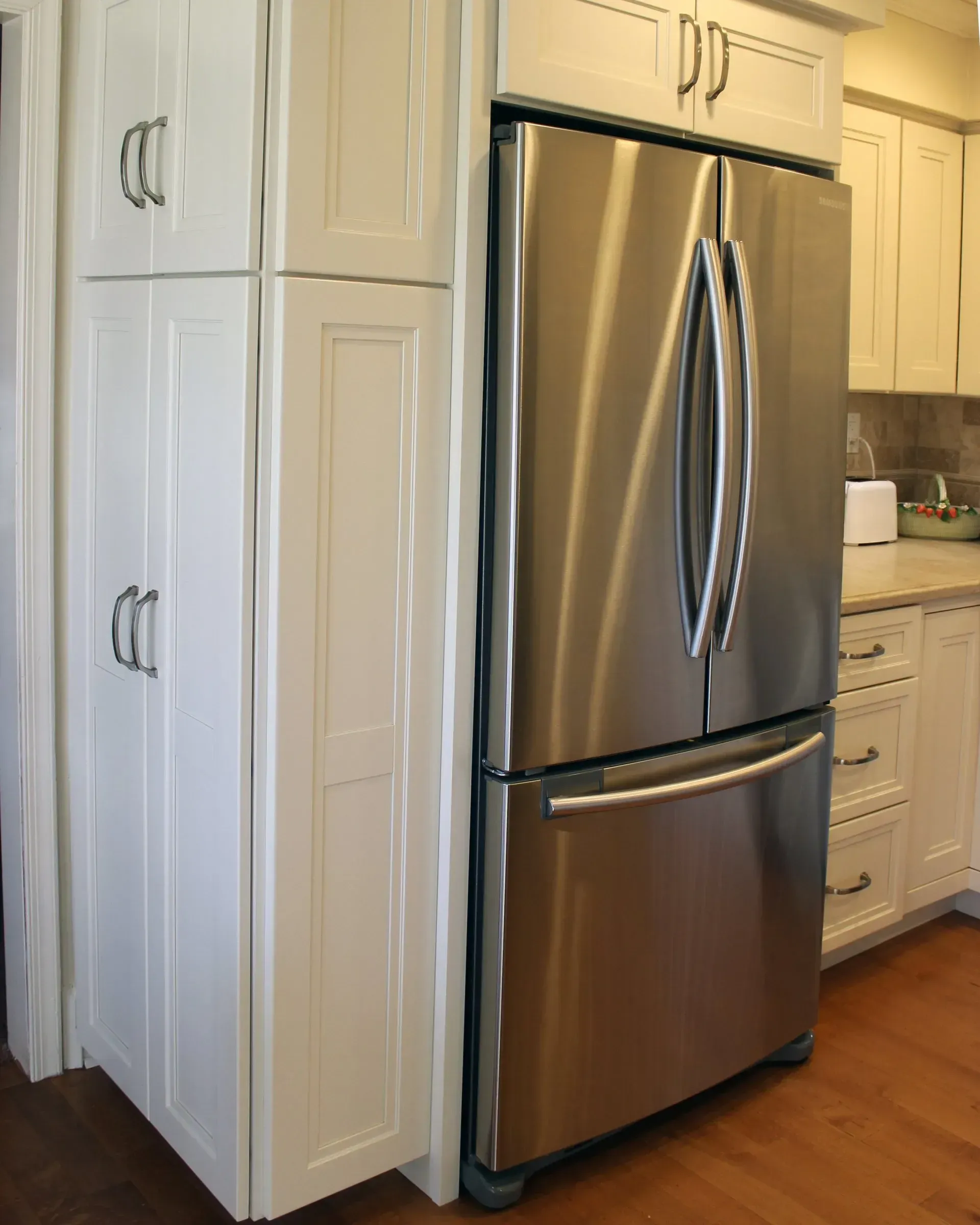 Stainless steel refrigerator in a bright kitchen with cream-colored cabinets and wood flooring In Bucks Country PA