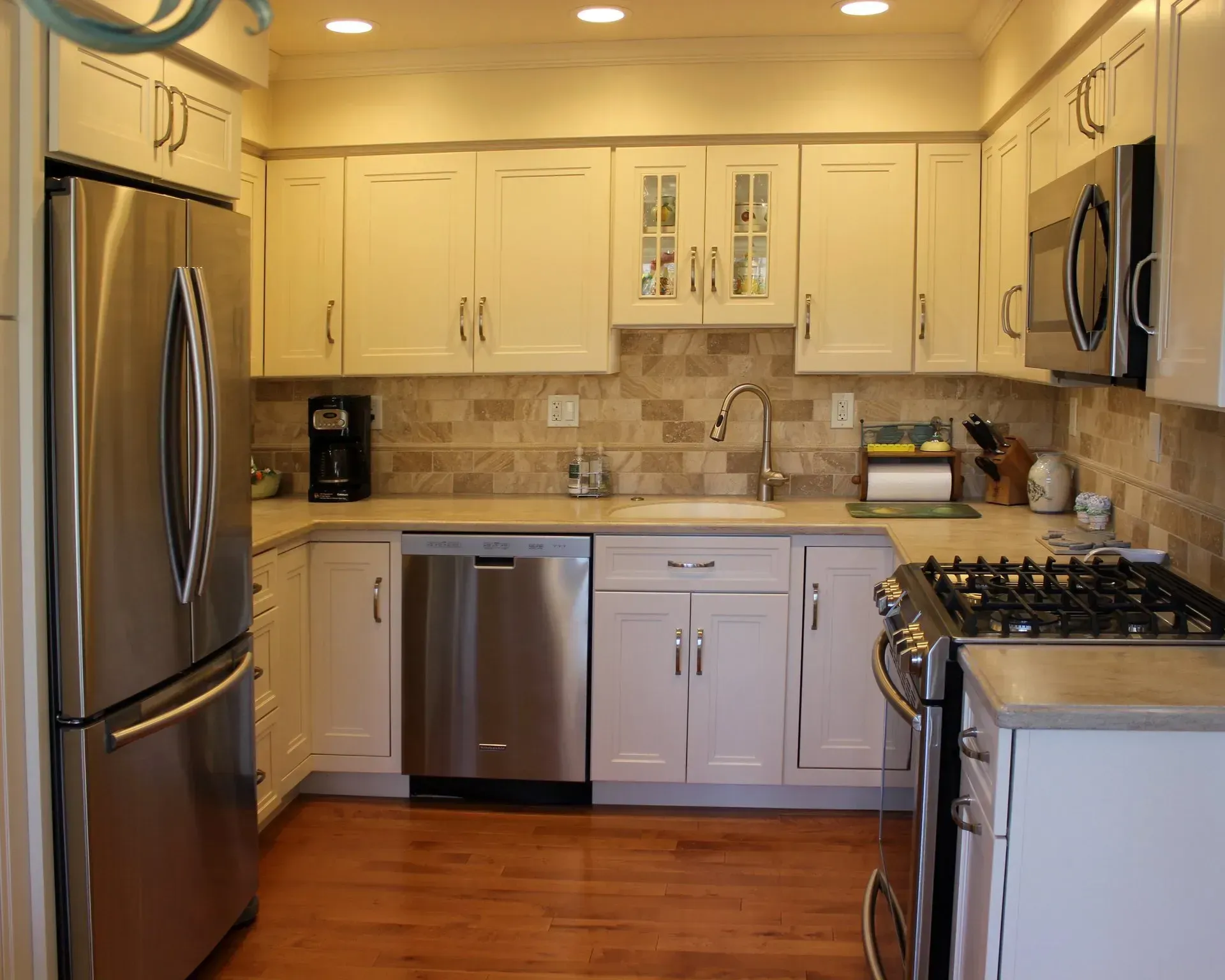 Modern kitchen with white cabinets, stainless steel appliances, tan tile backsplash, and hardwood floor In Bucks Country PA