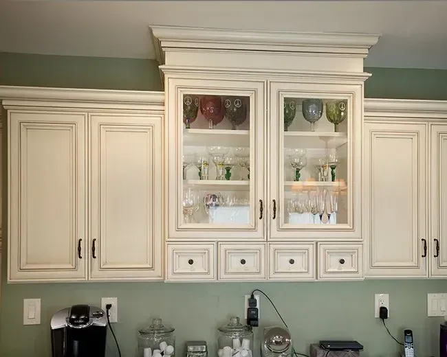 White kitchen cabinets with glass-front center display and countertop appliances below, against a green wall In Bucks Country PA
