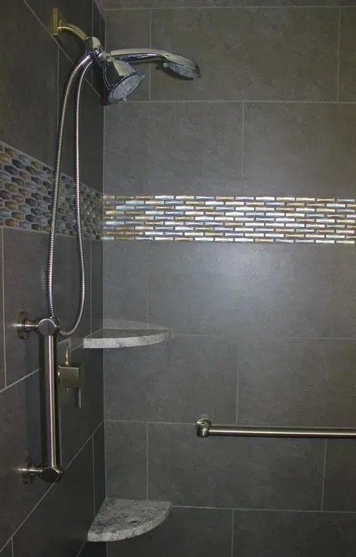 Walk-in shower with gray tile, handheld showerhead, and corner shelves in Bucks Country PA