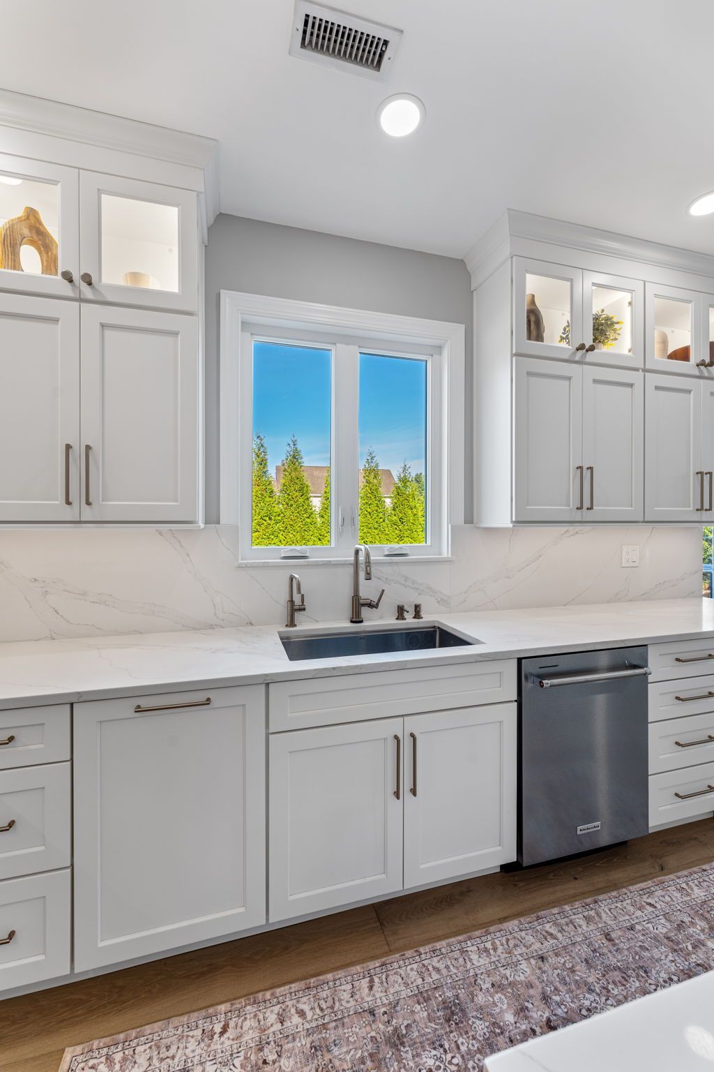 Bright white kitchen with gray cabinets, marble countertop, and window over the sink overlooking trees In Bucks Country PA