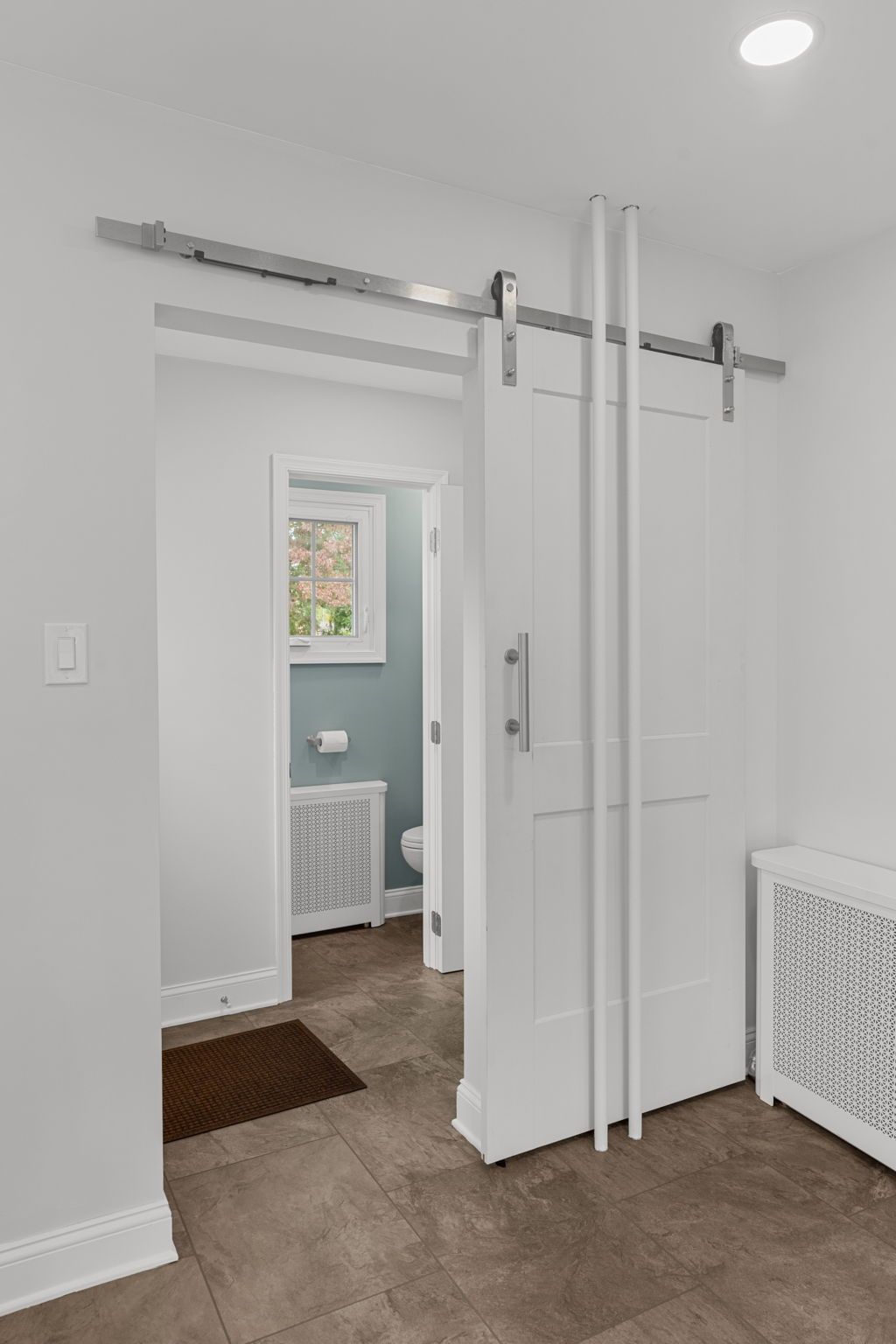 Interior doorway with sliding barn door hardware, white walls, and tan carpet leading to a bathroom in Bucks County PA