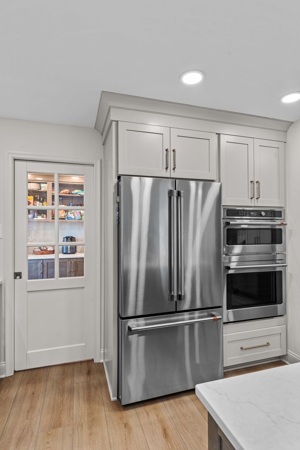 Modern kitchen with stainless steel fridge, built-in oven, white cabinets, and hardwood floor in Bucks County PA