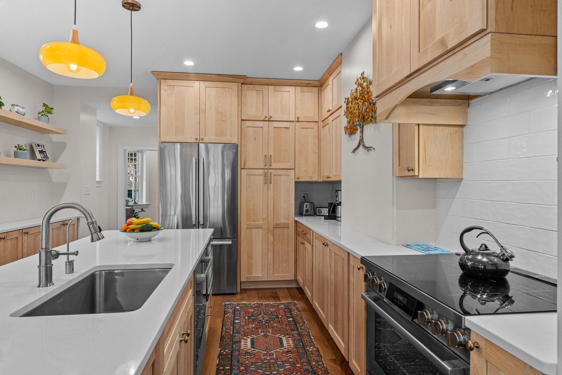 Bright modern kitchen with light wood cabinets, stainless fridge, white counters, and yellow pendant lights In Bucks County PA
