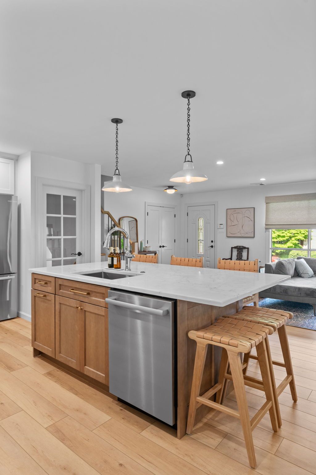 Modern kitchen with white island, stainless dishwasher, wooden stools, pendant lights, and bright windows In Bucks County PA